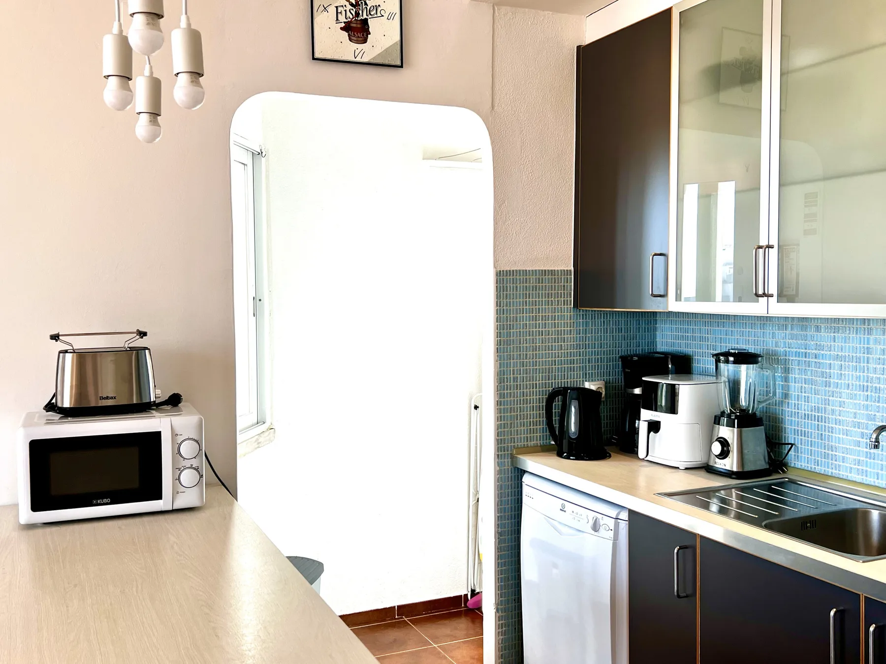 Una cocina luminosa con electrodomésticos sobre la encimera, armarios oscuros y un salpicadero de azulejos.
