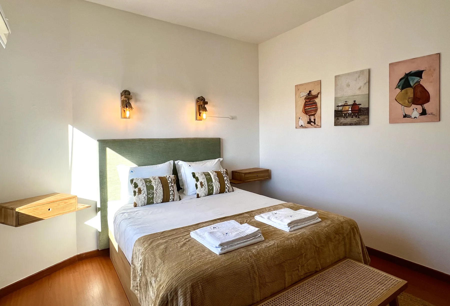 Un dormitorio con una cama bien hecha, mesitas de noche y cuadros en la pared.