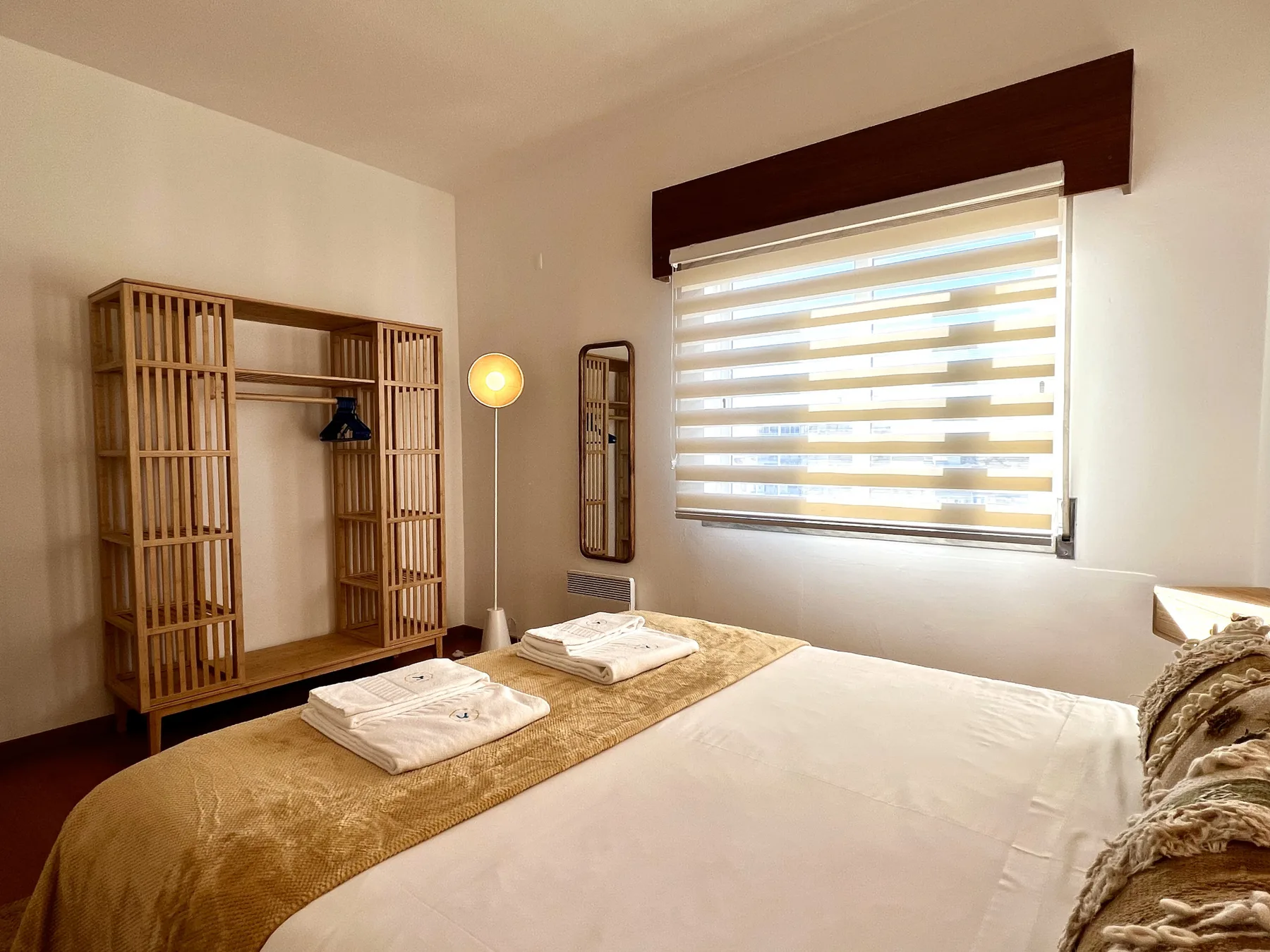 Dormitorio con una cama, toallas dobladas y un armario de madera junto a la ventana.