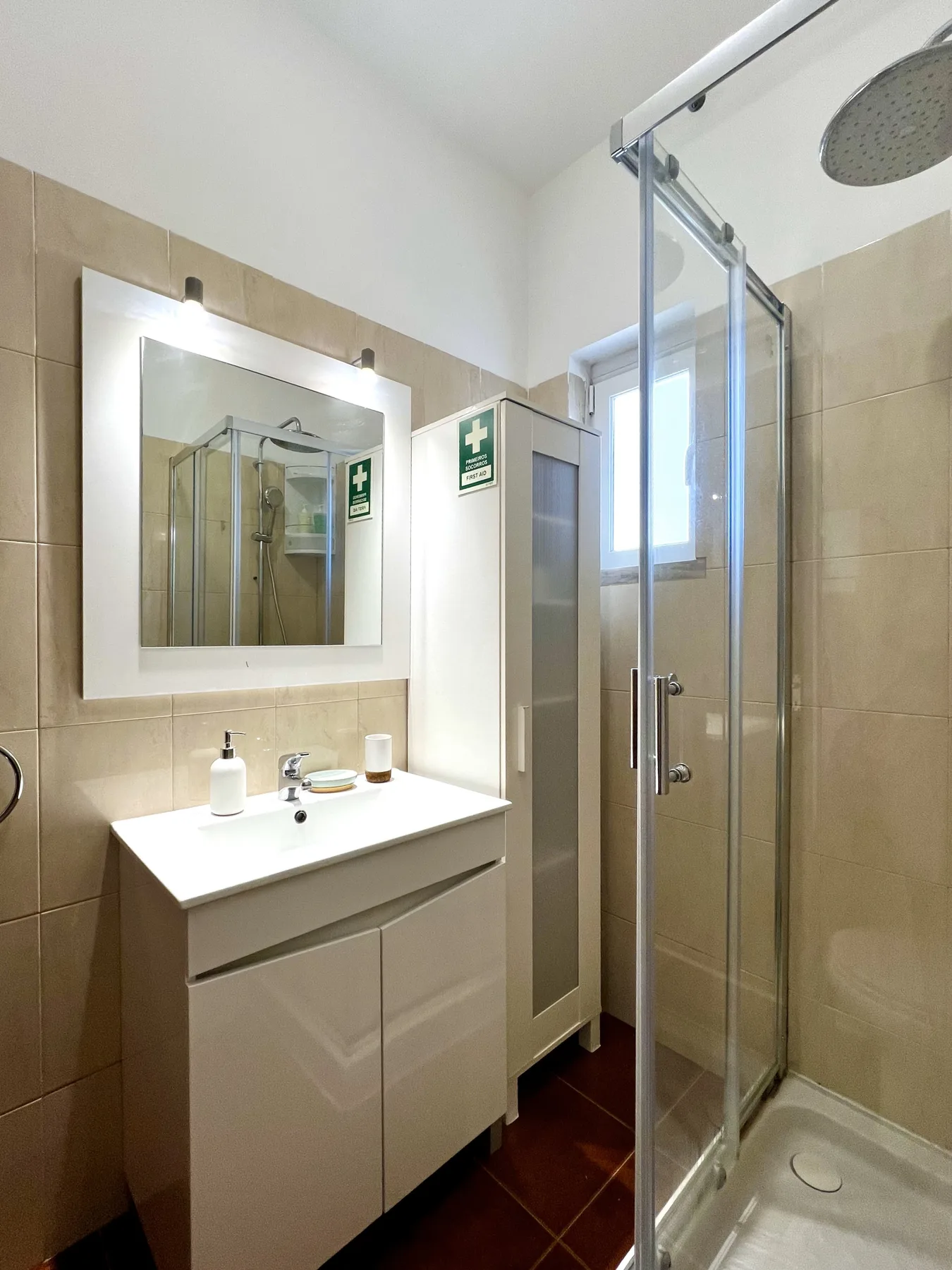 Un baño alicatado con mueble de lavabo blanco, espejo de pared y ducha de cristal.