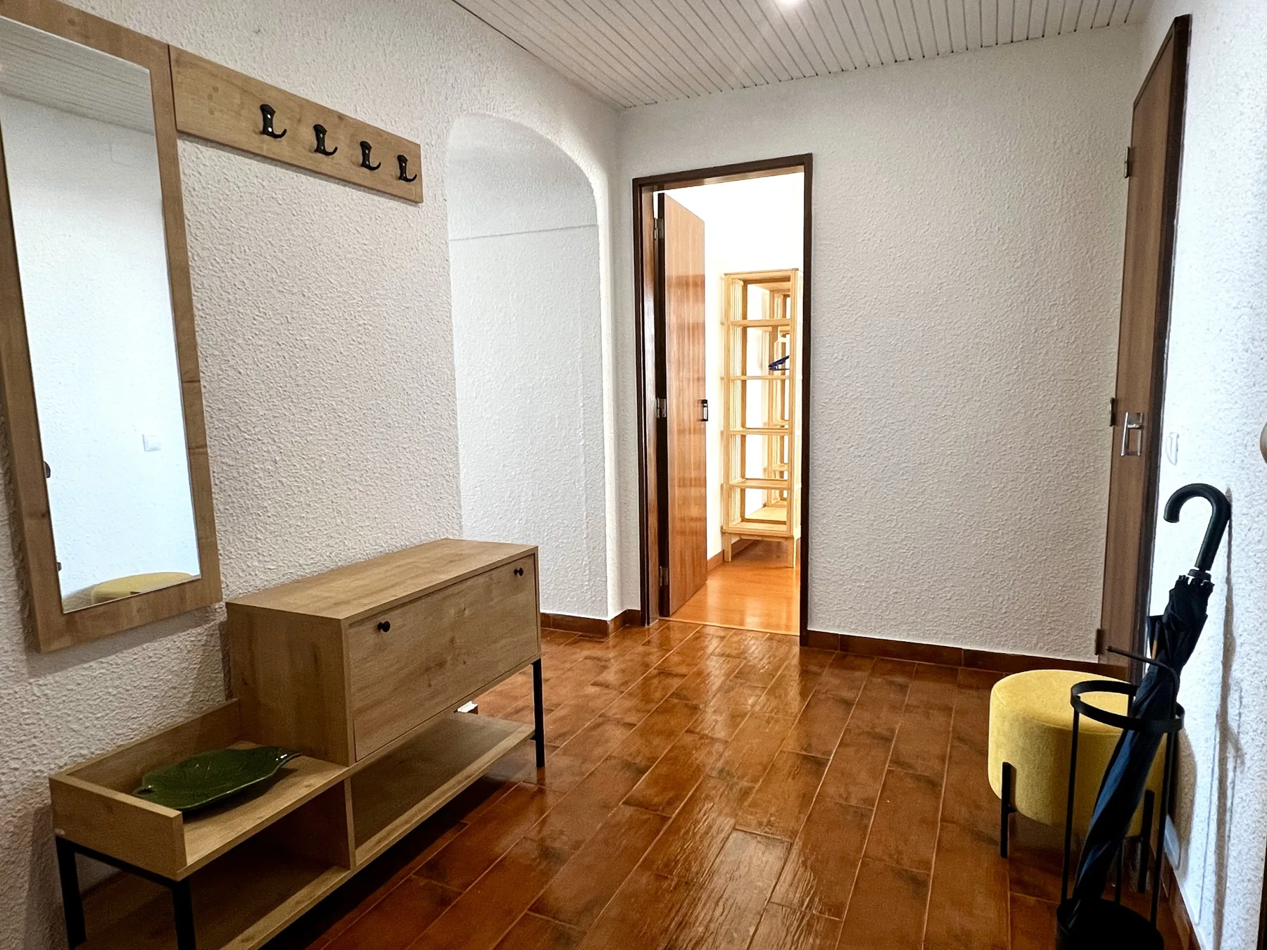 Entrada de un apartamento con una consola de madera y una puerta que da a otra habitación.