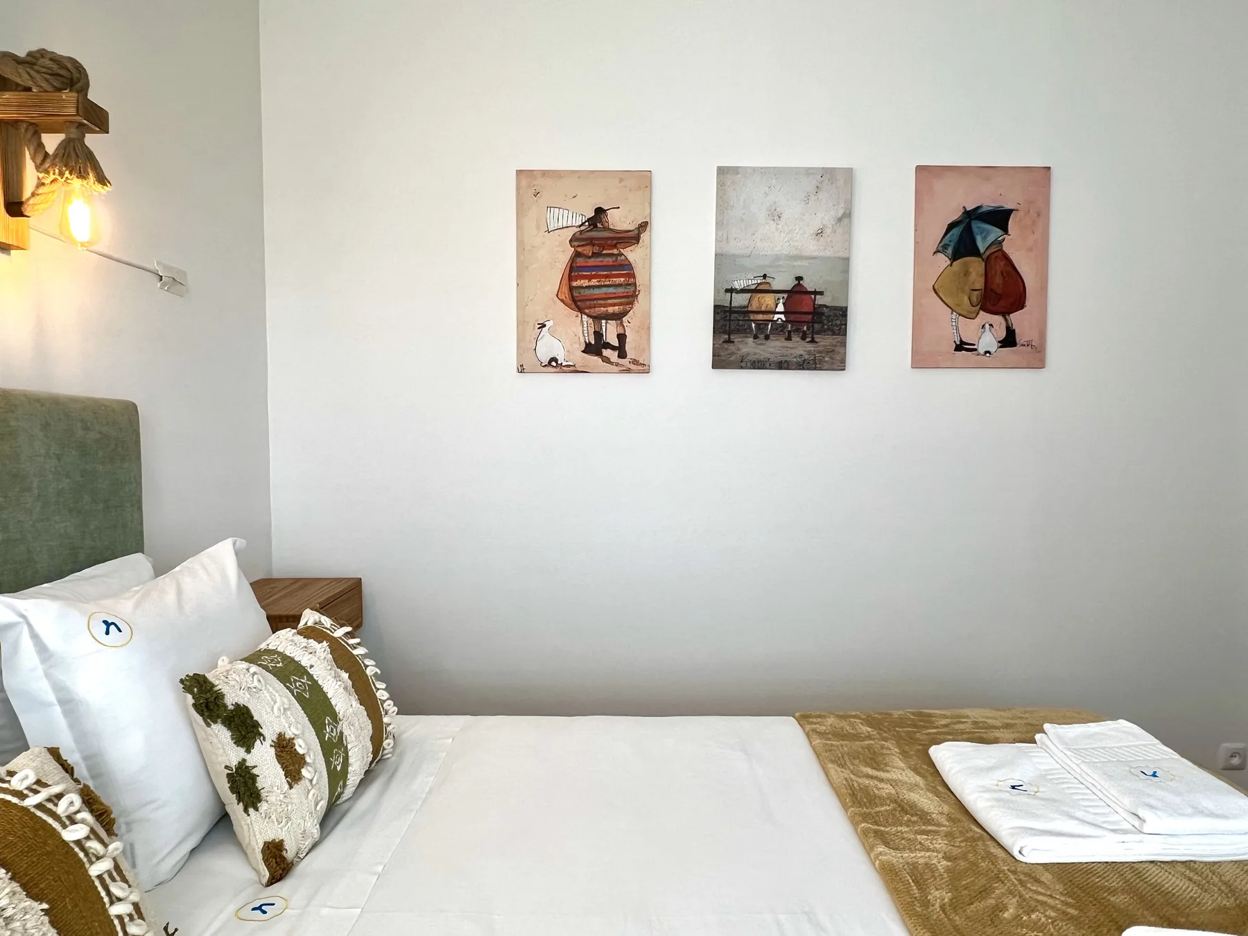 Un dormitorio con una cama bien arreglada y tres cuadros en la pared.