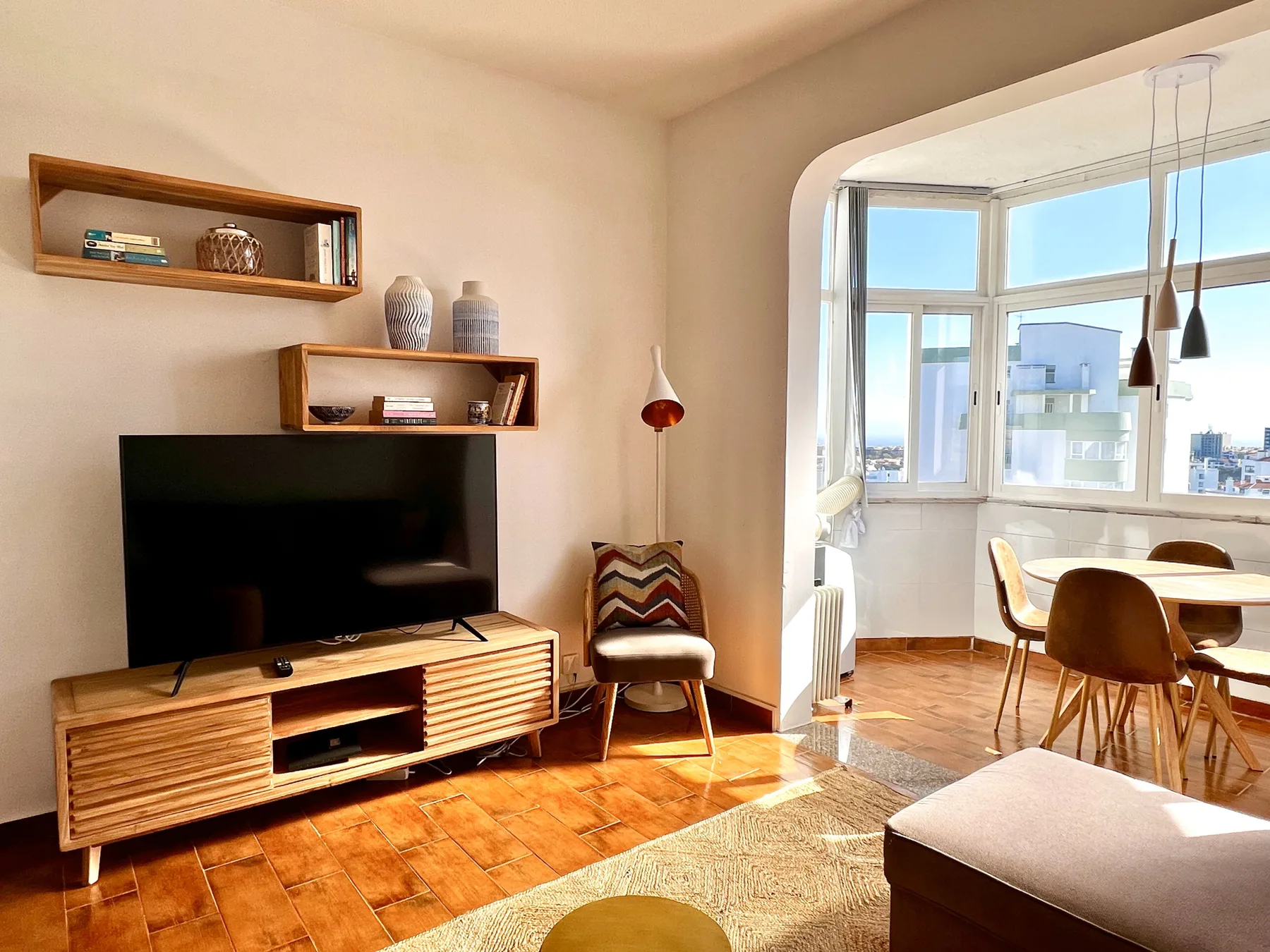 Una zona de estar y comedor con televisor, asientos y grandes ventanales.