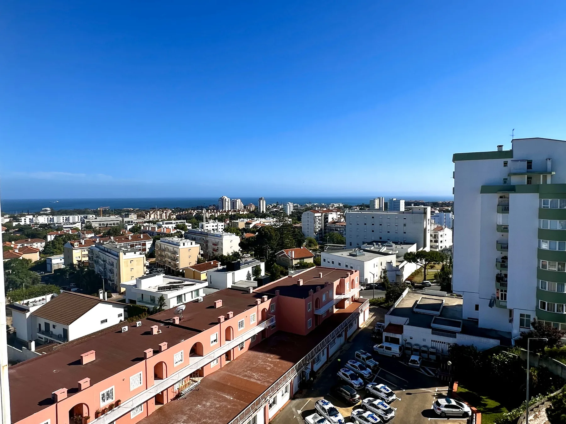 Un paisaje urbano costero con edificios, coches aparcados y el océano en el horizonte.