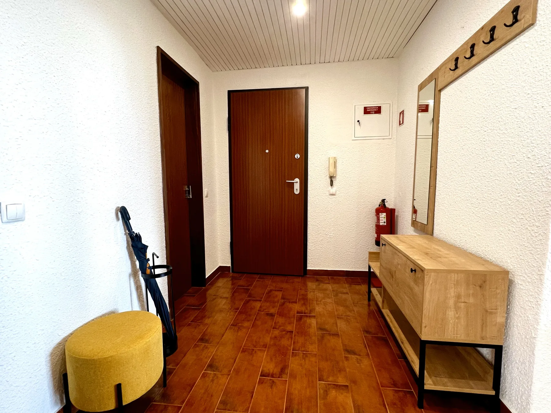 Un recibidor de apartamento con una puerta de madera, un banco y ganchos en la pared.