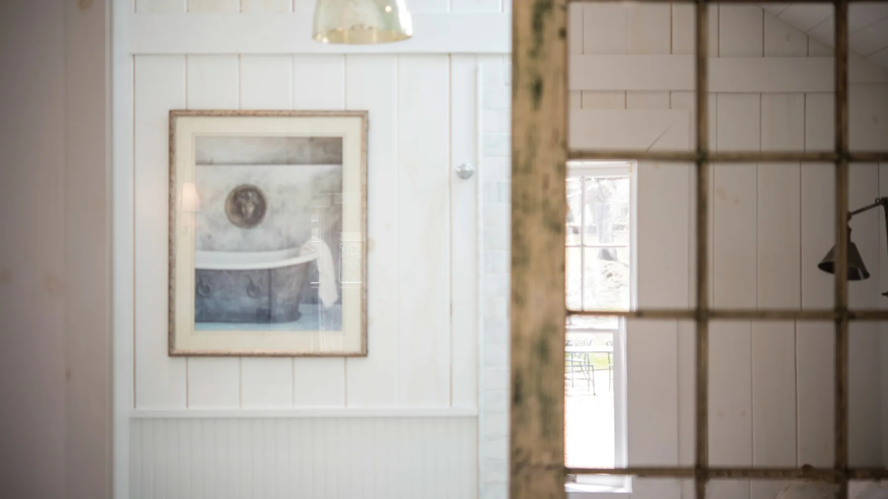 A bright interior with white paneled walls, framed artwork, and a large gridded window.