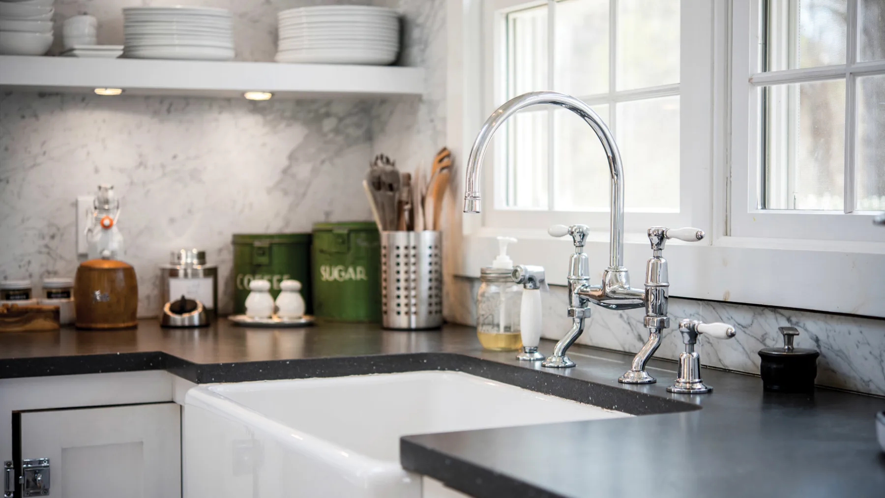 A bright kitchen counter with a large white sink and chrome faucet beneath the windows.