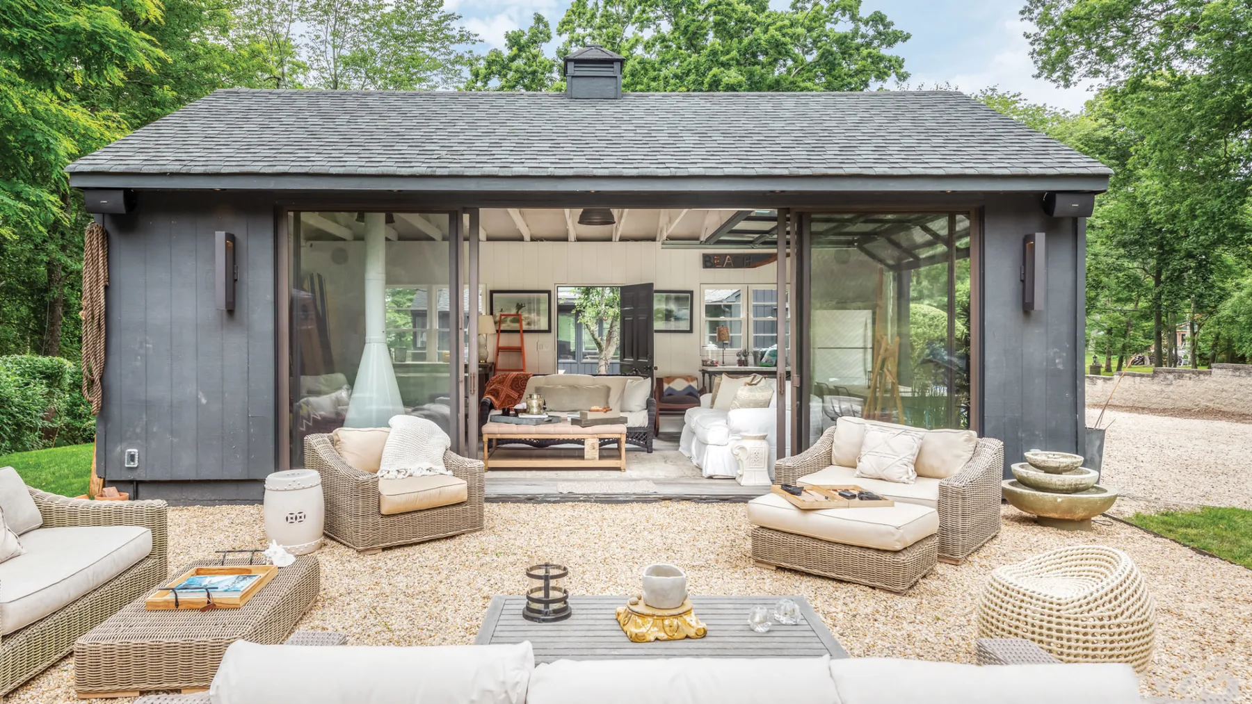 A patio seating area faces a house with wide glass doors and surrounding greenery.
