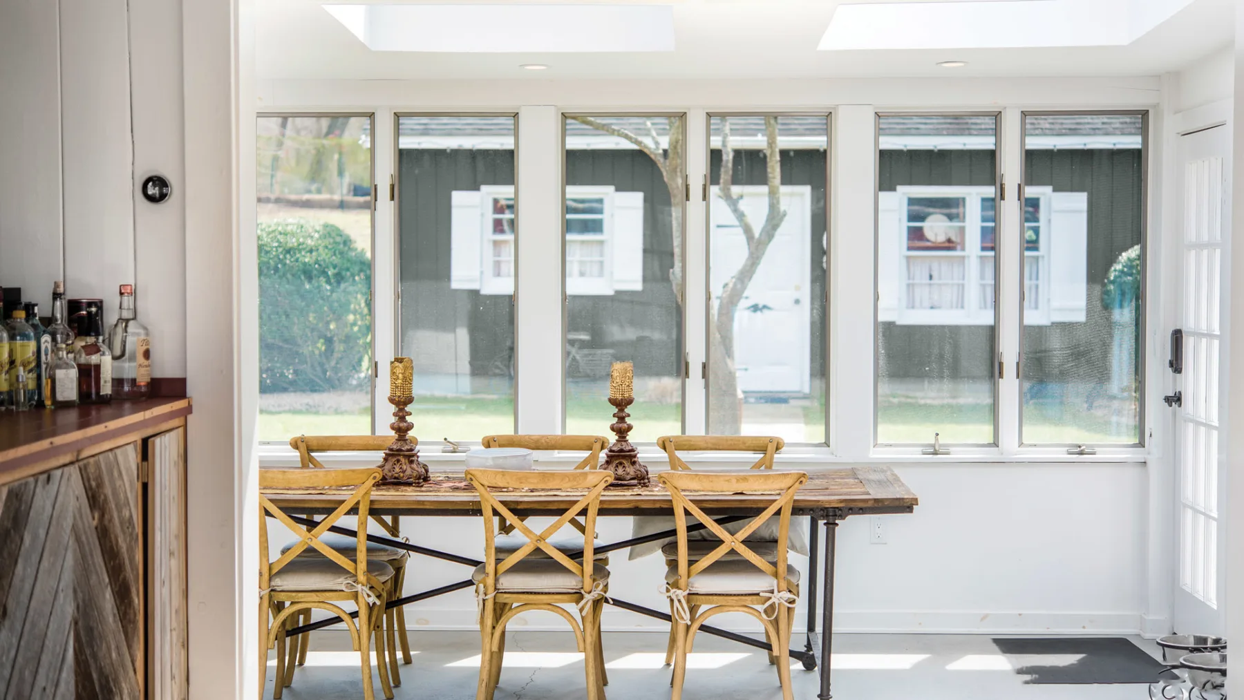 A bright dining area with a long table and wooden seating beside large windows.
