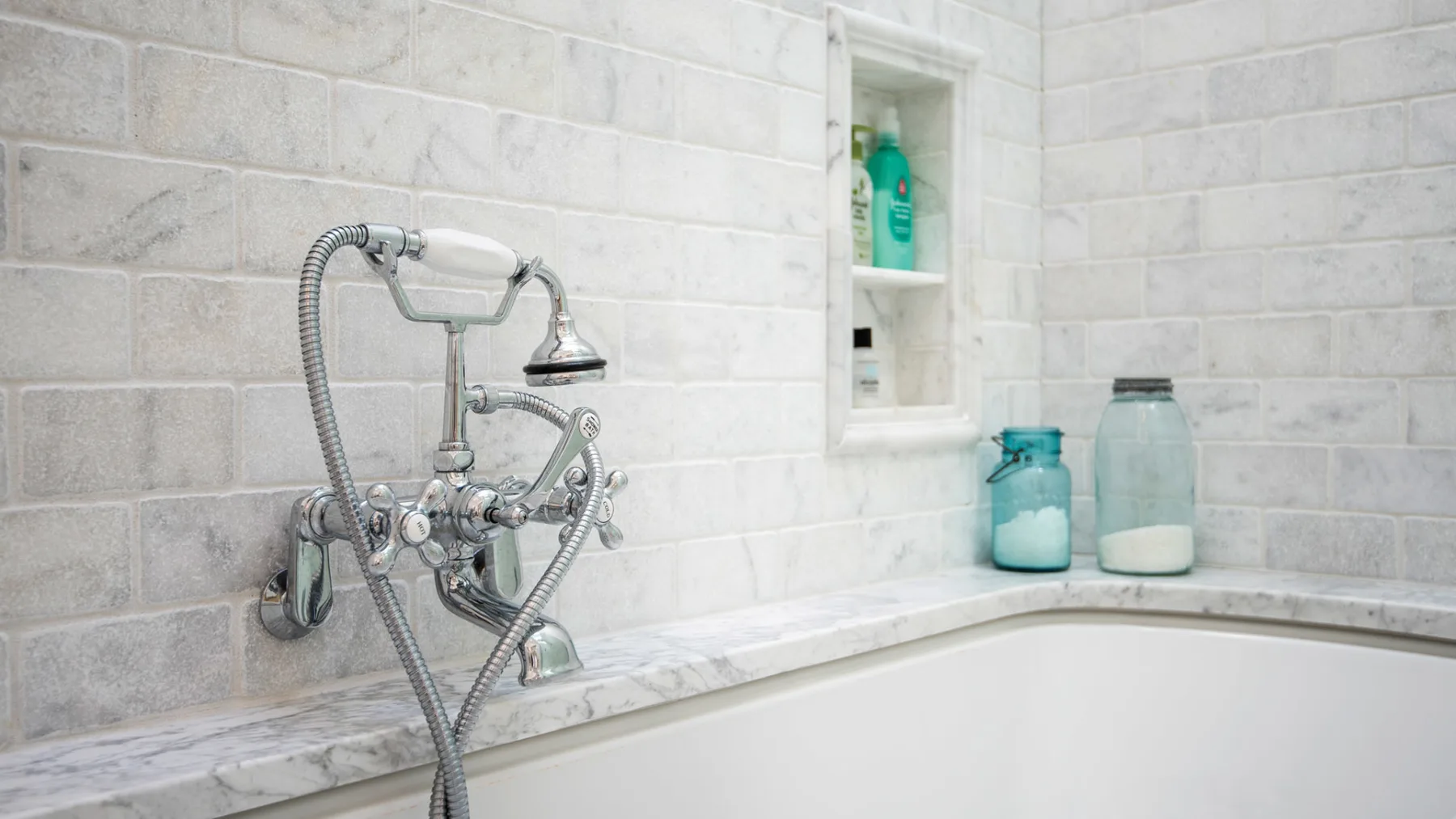 A tiled bathroom wall features a bathtub and wall-mounted shower fixtures.