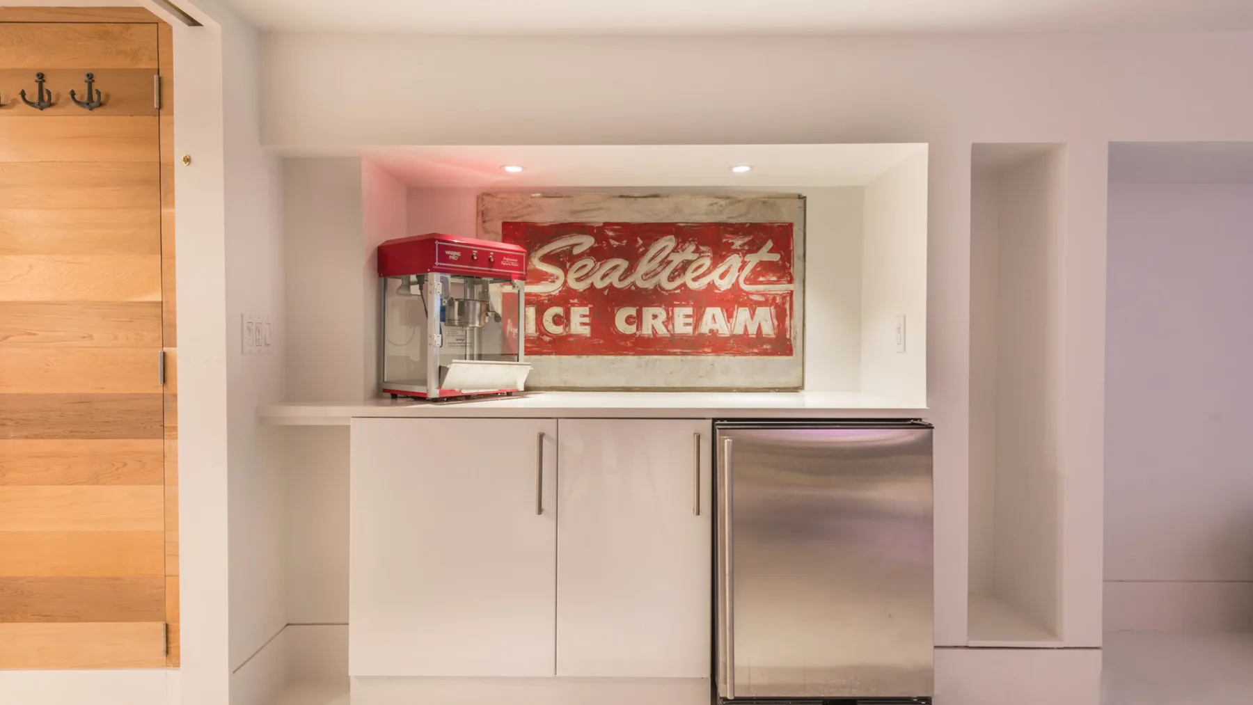 A built-in refreshment counter with a red popcorn machine and a stainless-steel refrigerator.