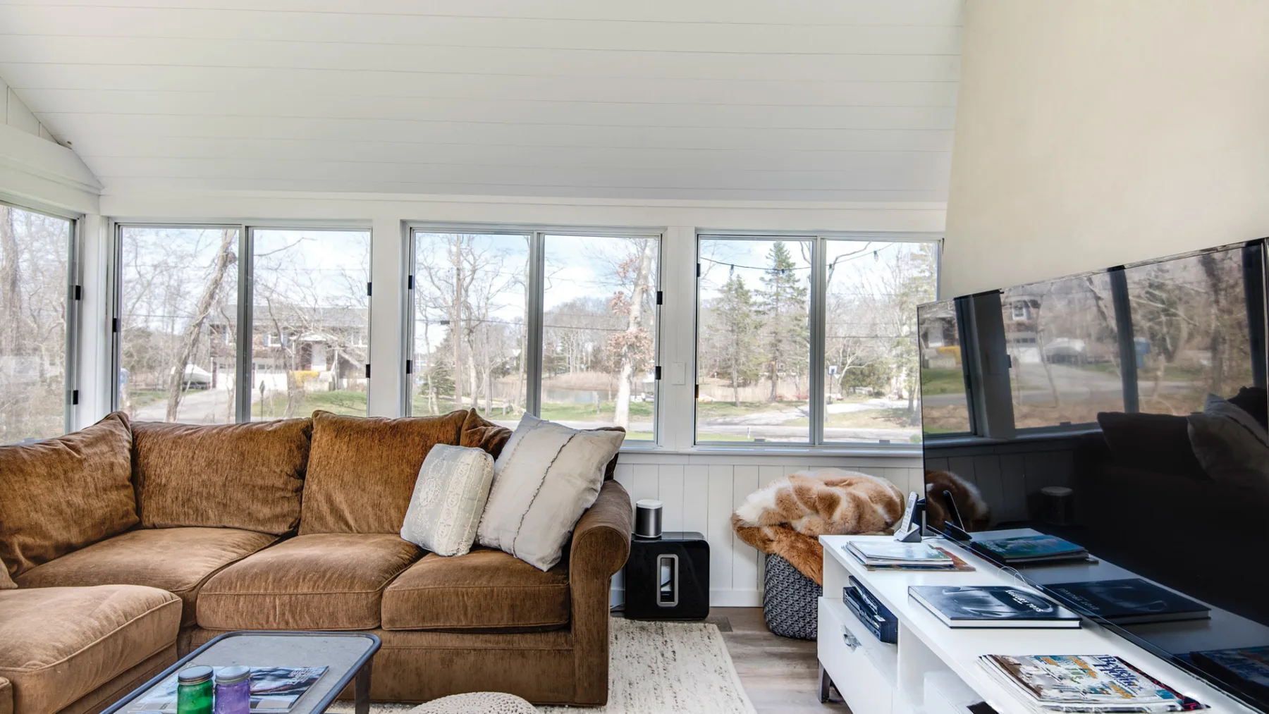 A bright living room with seating, large windows, and a television.