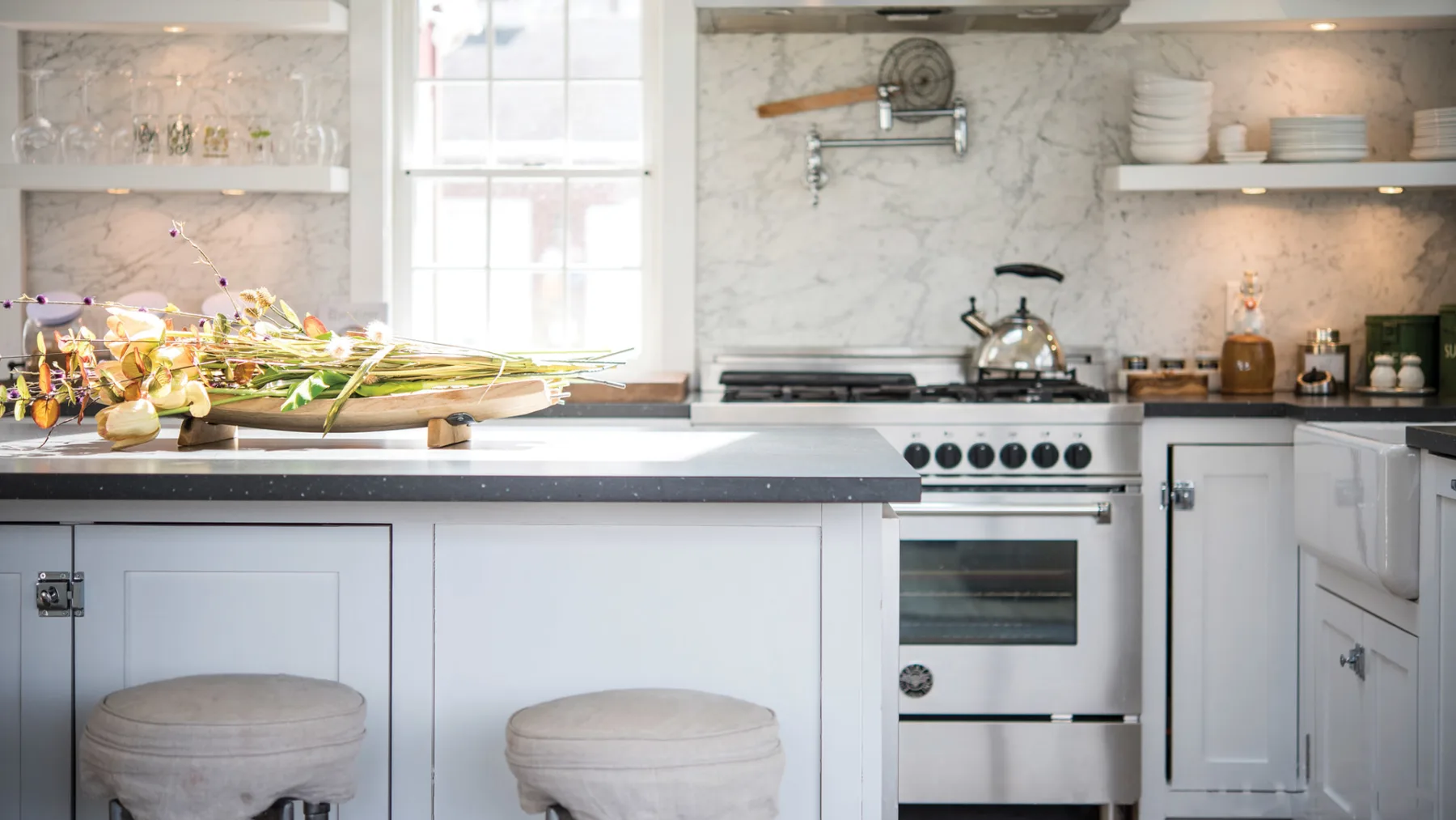 A bright kitchen with a countertop island and a stove beneath open shelves.