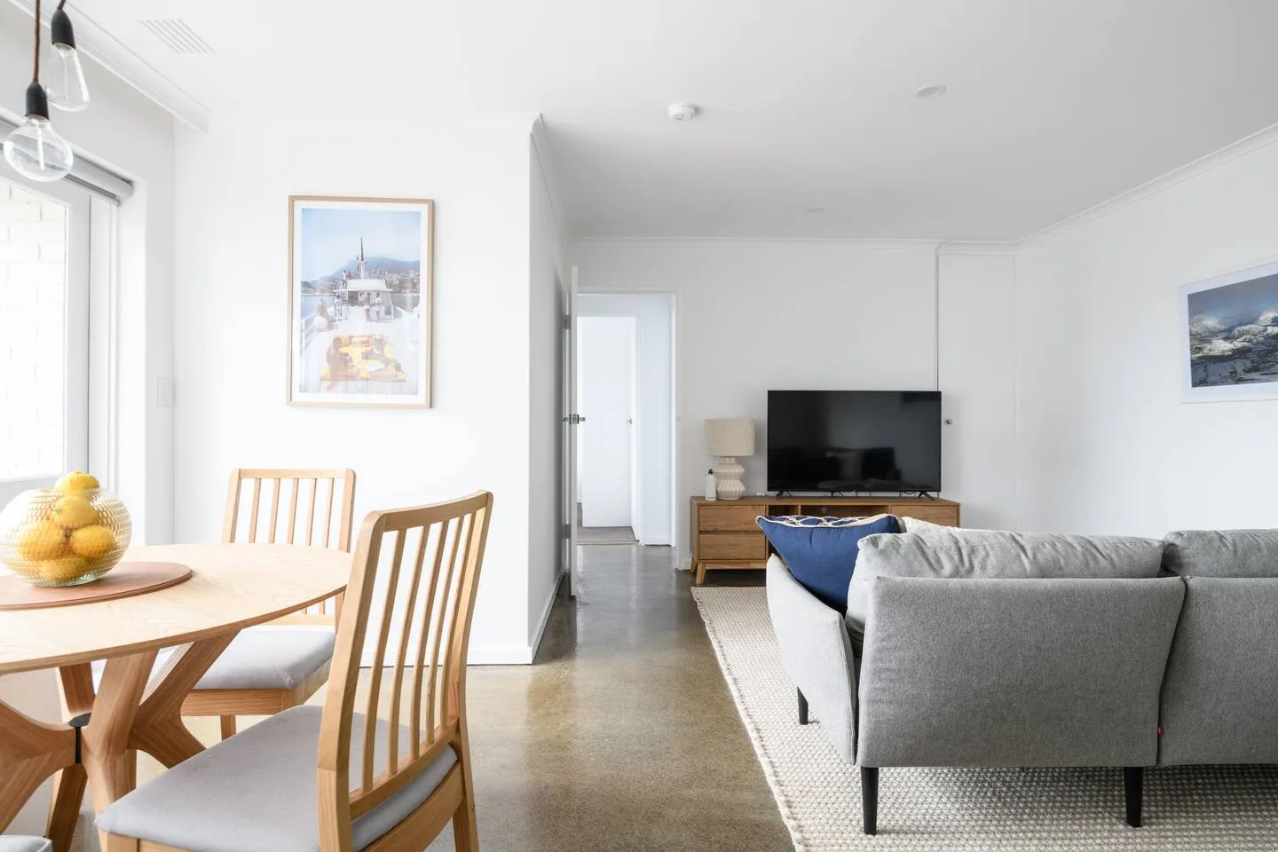 A bright living and dining area with a television and light-colored seating.