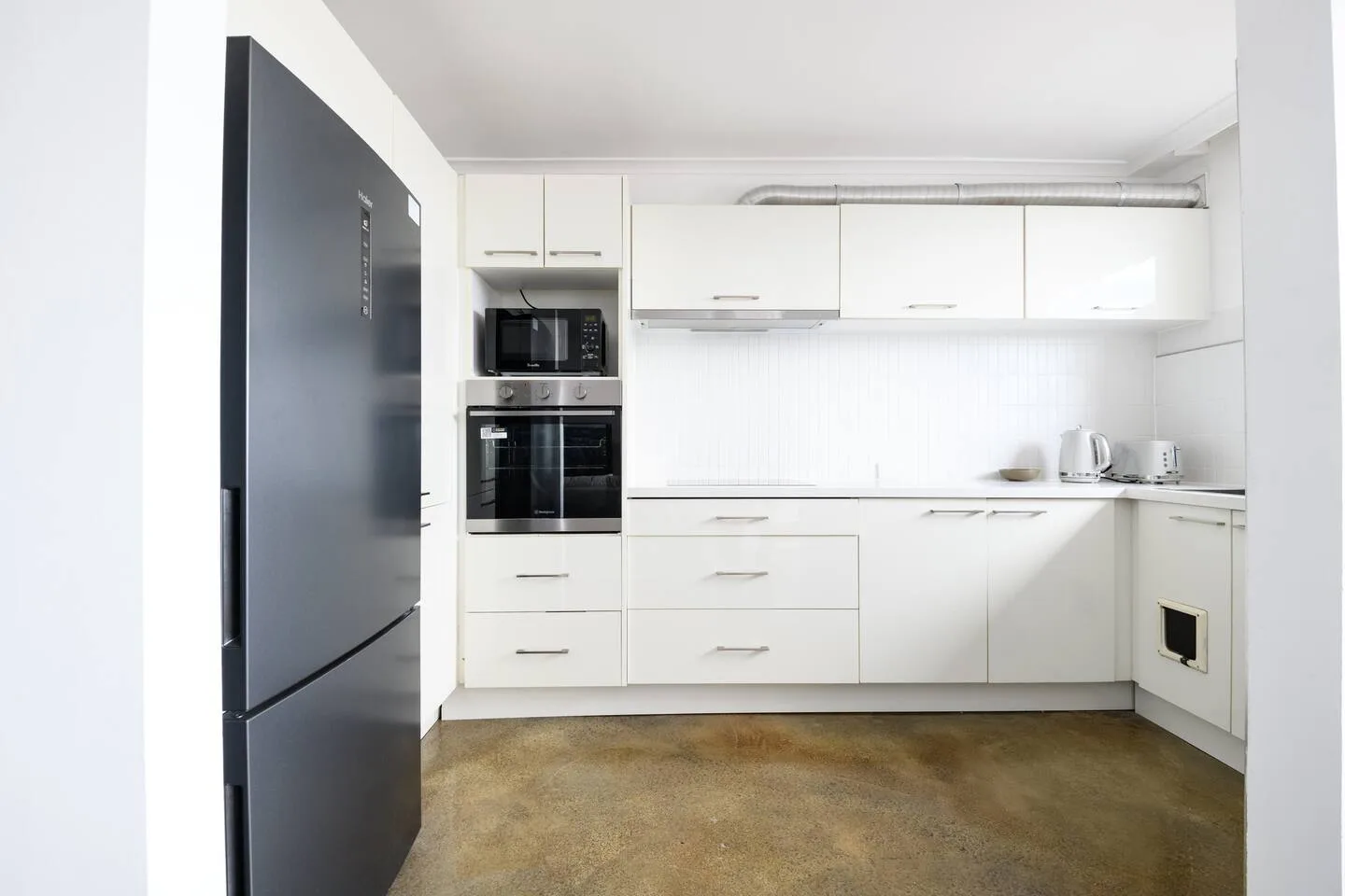 A bright white kitchen with built-in appliances and a long countertop.