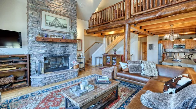 A living room with a stone fireplace, seating, and a wooden loft railing.