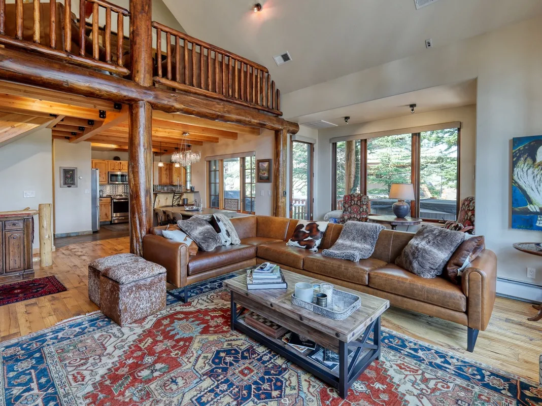 A spacious living room with a leather seating area beneath a wooden balcony.