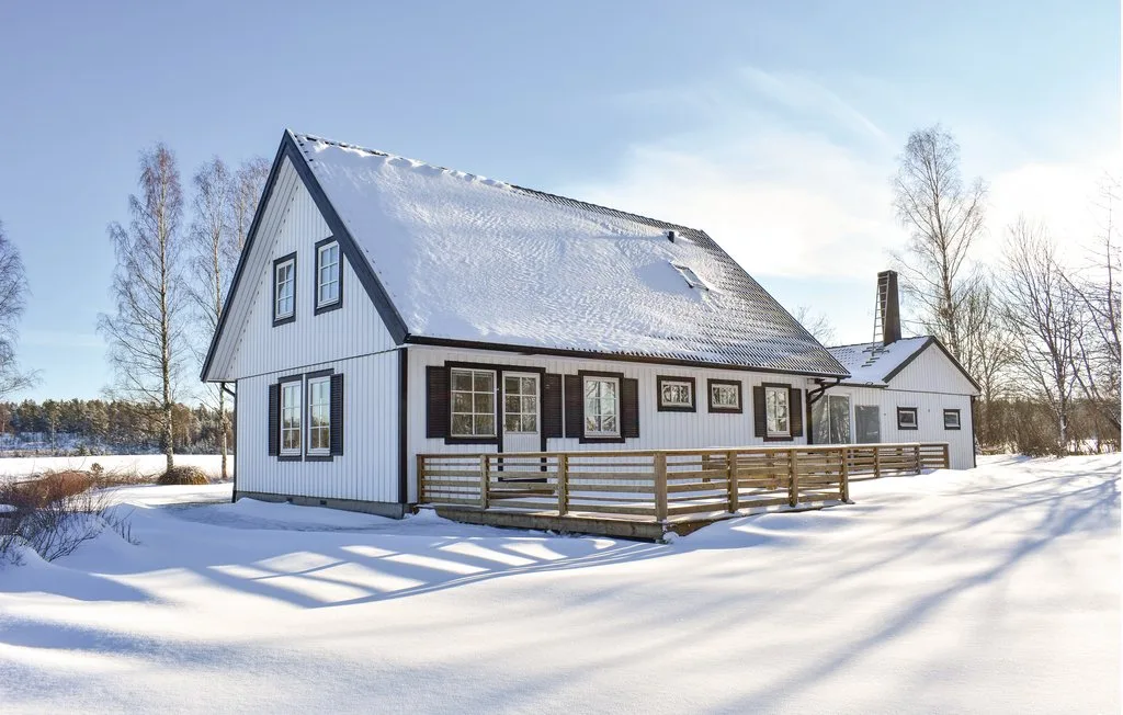 A white house stands in a snow-covered landscape beside a wooden deck.