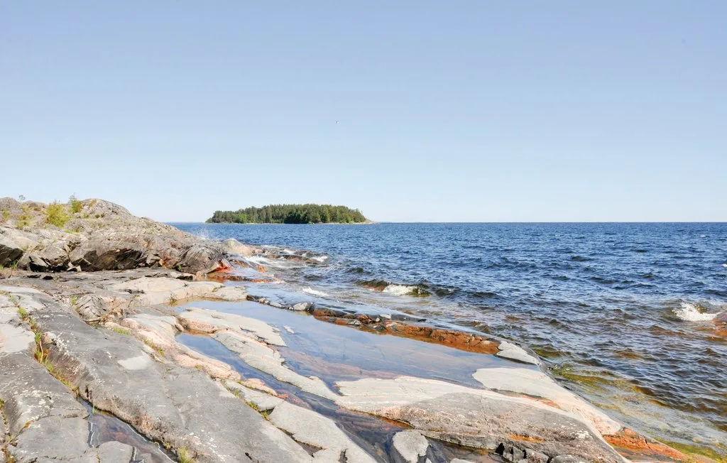 A rocky shoreline slopes into a blue lake beneath a clear sky.