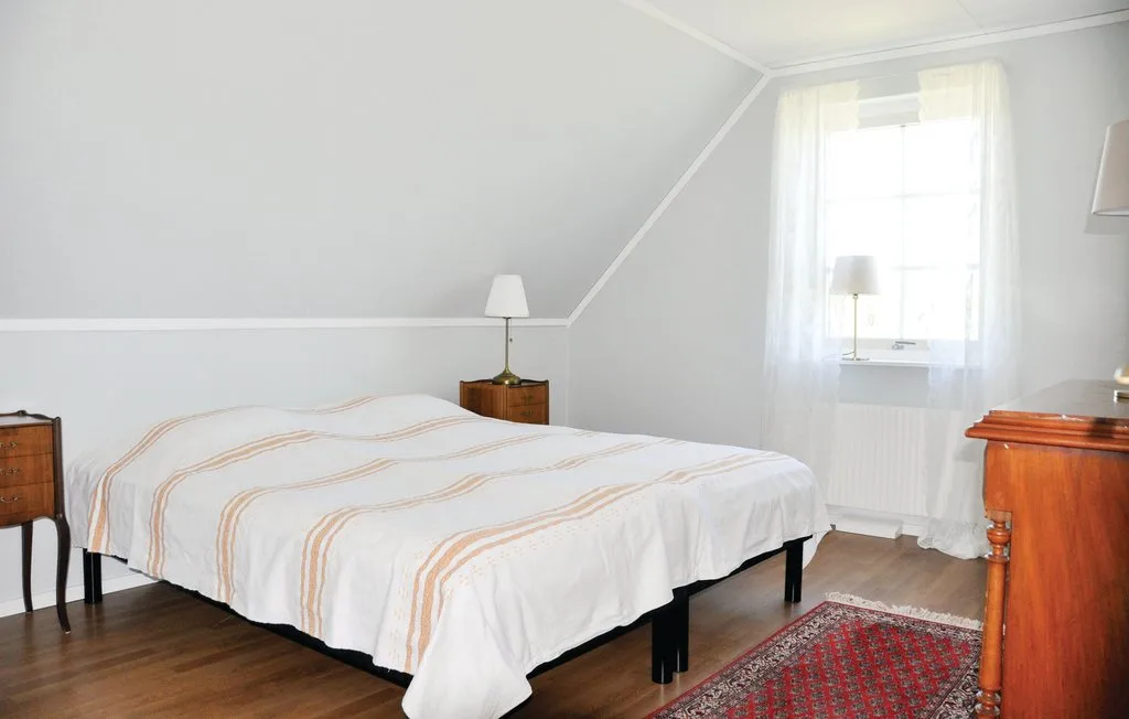A bedroom with a bed beneath a sloped ceiling and a bright window.
