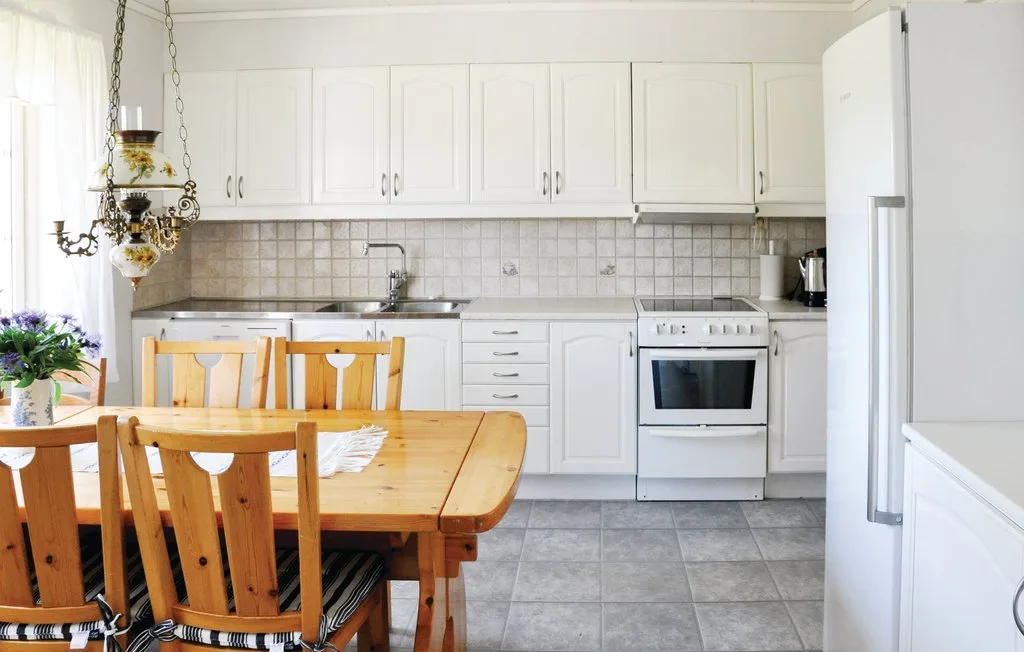 A bright kitchen with white cabinets, a tiled backsplash, and a wooden dining table.