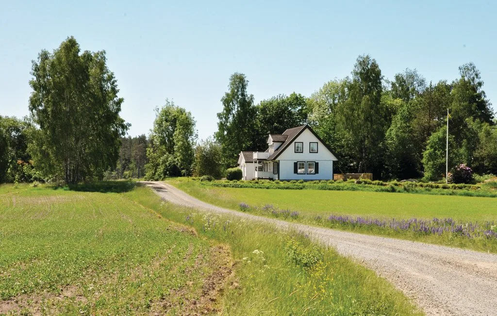 A house stands beside a gravel driveway amid green fields and trees.