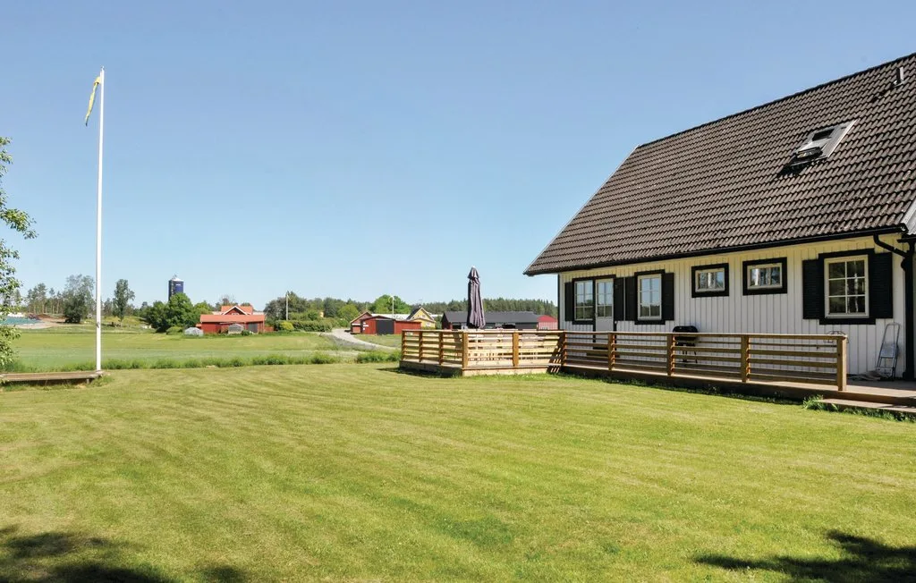 A house stands beside a broad grassy lawn and wooden deck.