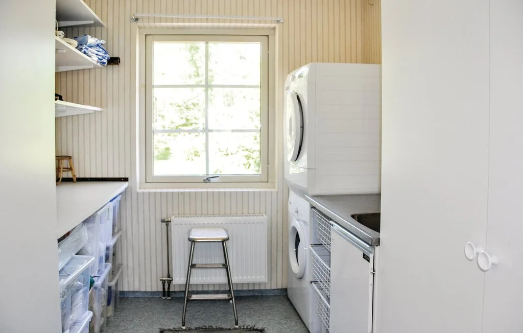 A laundry room with stacked appliances, open shelving, and a window.