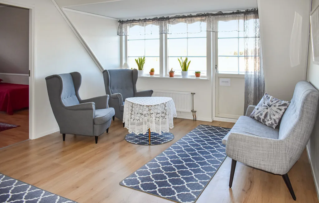 A bright sitting room with upholstered seating, a lace-covered table, and large windows.