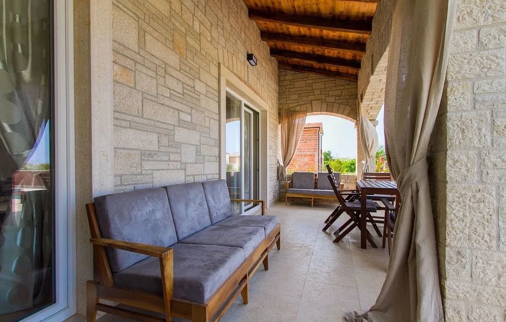 Un patio cubierto tiene asientos acolchados y una mesa de comedor bajo un techo de madera.