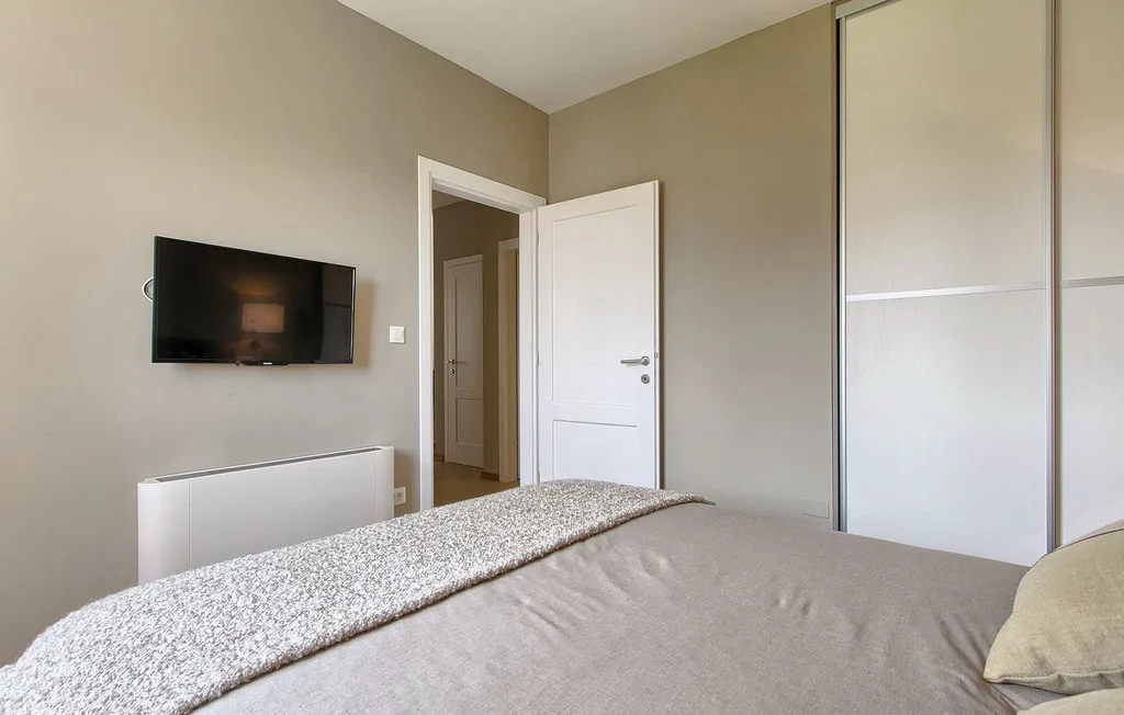 Un dormitorio con una cama, un televisor en la pared y una puerta abierta.