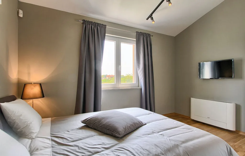 Un dormitorio con una cama bien tendida, una ventana y un televisor en la pared.
