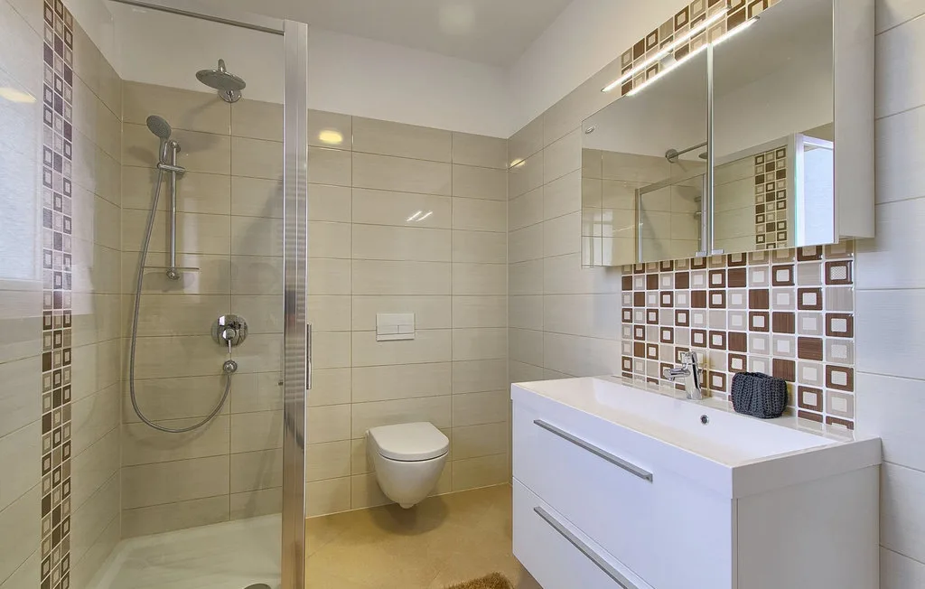 Un baño moderno con ducha de vidrio, inodoro suspendido y lavabo con mueble.