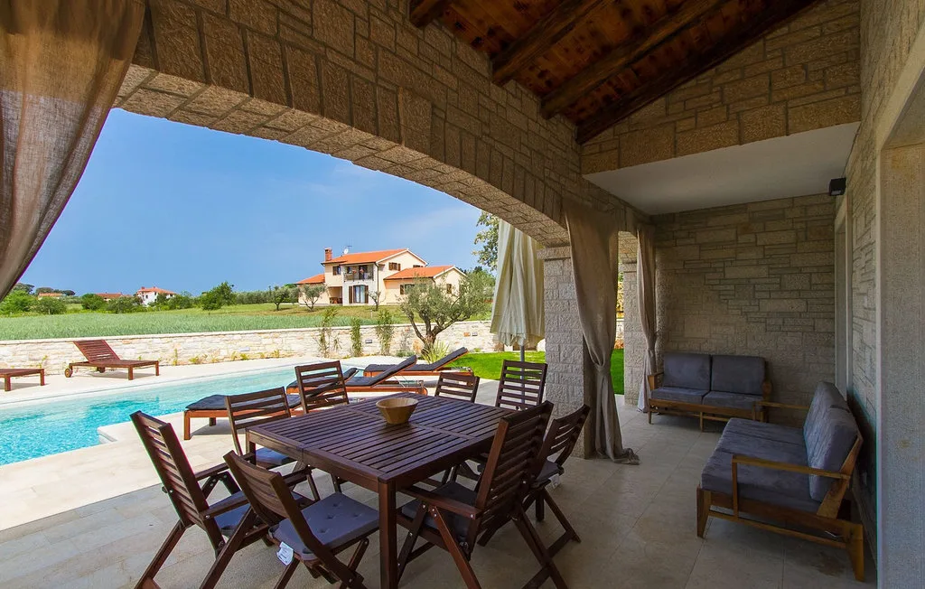 Un patio cubierto tiene una mesa de comedor de madera junto a una piscina.