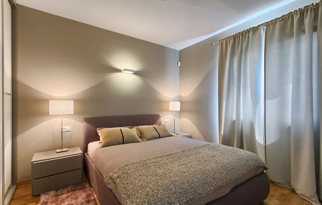 Un dormitorio con una cama, mesitas de noche y cortinas que cubren la ventana.