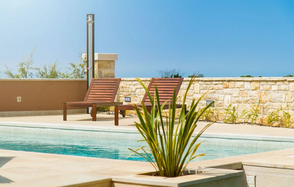 Una piscina exterior está junto a tumbonas de madera y un muro bajo de piedra.