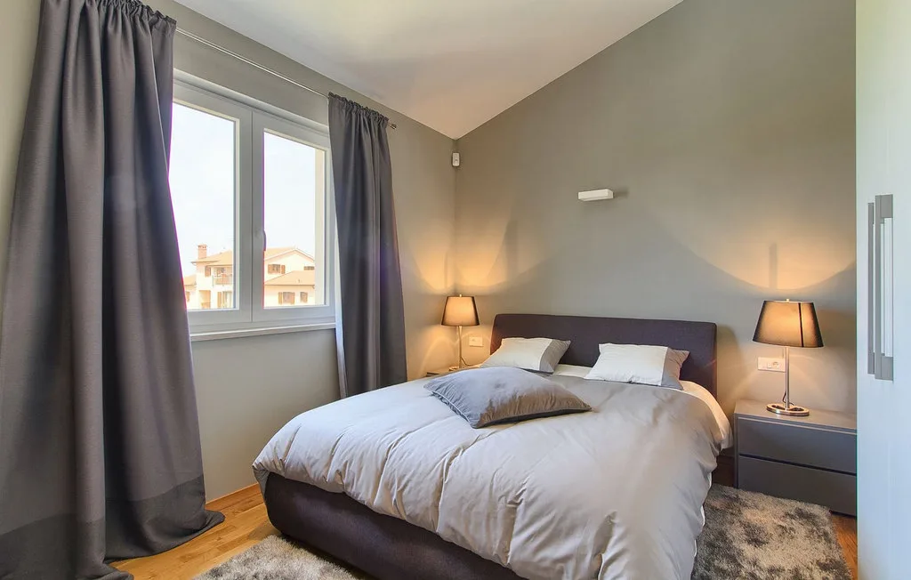 Un dormitorio con cama, mesitas de noche y una ventana con cortinas.