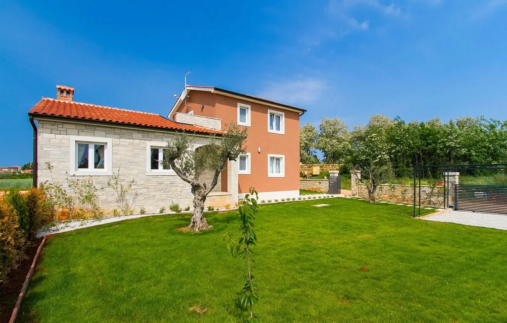 Una casa se encuentra junto a un césped verde, con árboles y una zona cercada.