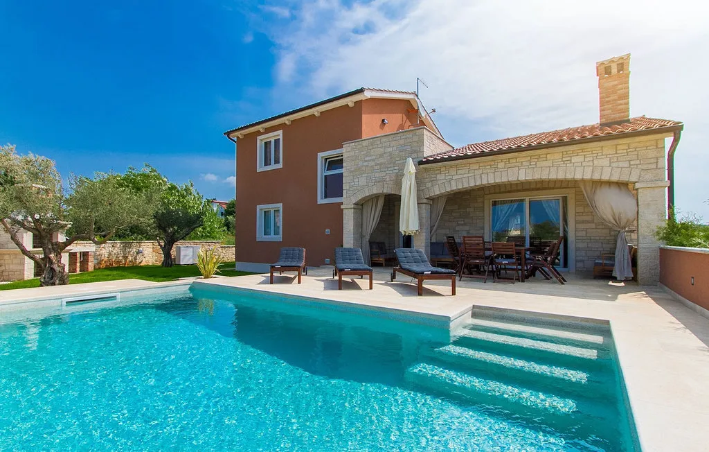 Una piscina junto a una casa, con asientos en el patio bajo una zona cubierta.