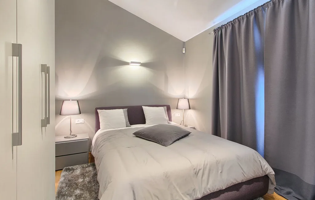 Un dormitorio con una cama bien tendida, mesillas de noche y cortinas oscuras.