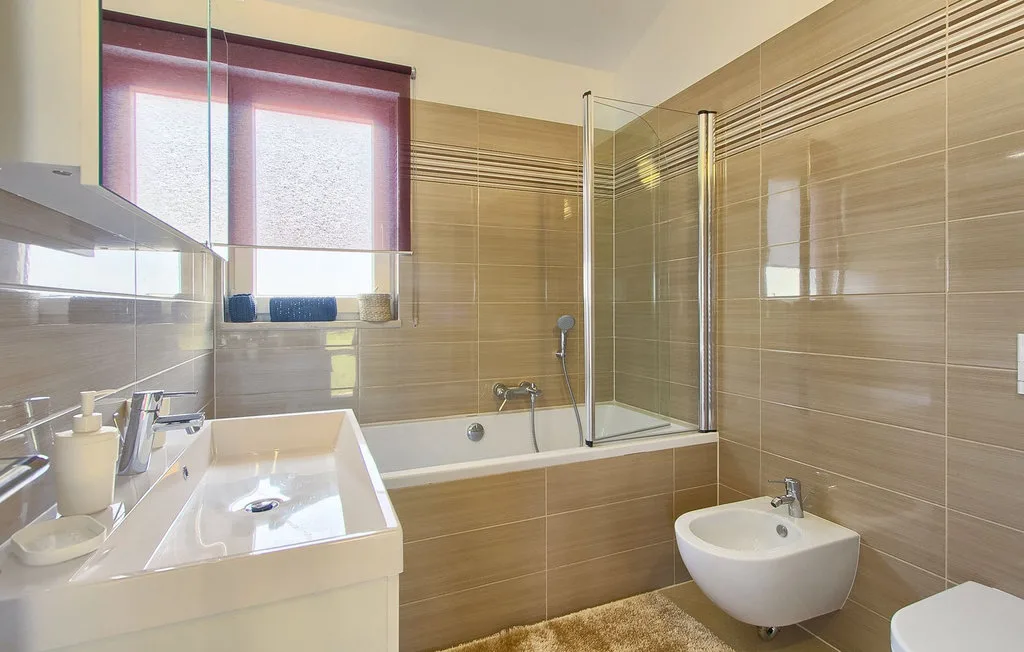 Un baño con bañera, mampara de cristal y lavabo suspendido.
