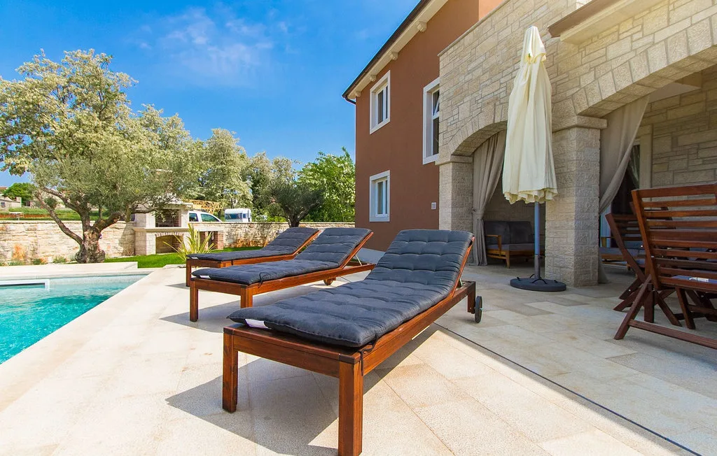 Un patio junto a la piscina con tumbonas acolchadas junto a un edificio revestido de piedra.