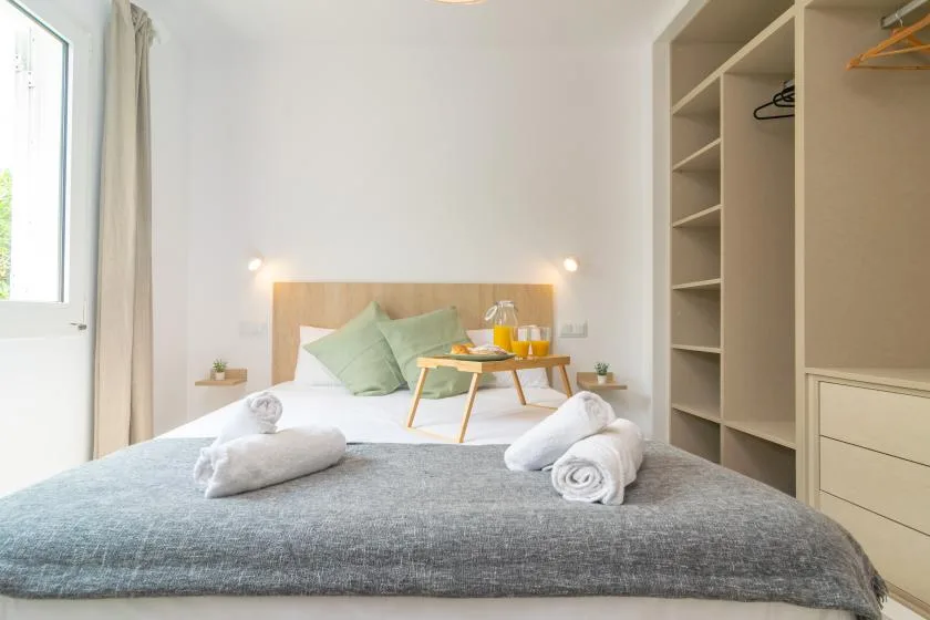 A bright bedroom with a neatly made bed and open wardrobe shelving.