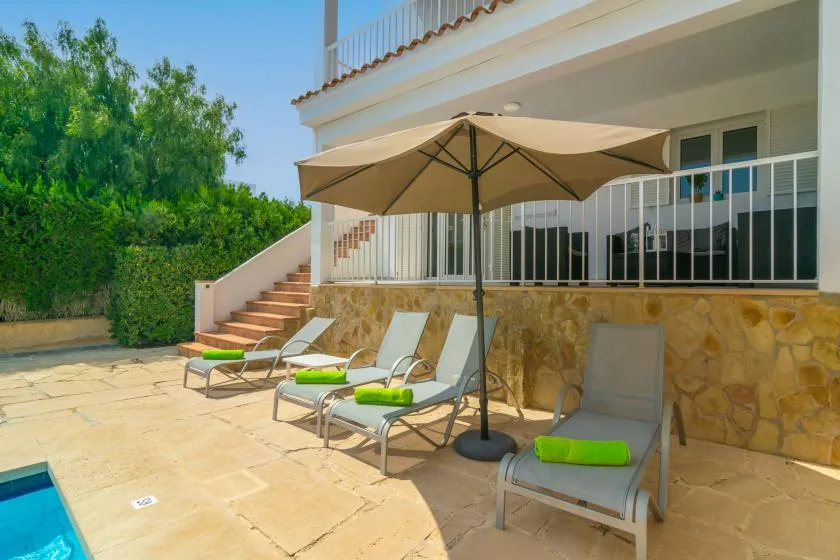 Un patio soleado con asientos reclinables y una gran sombrilla junto a la casa.