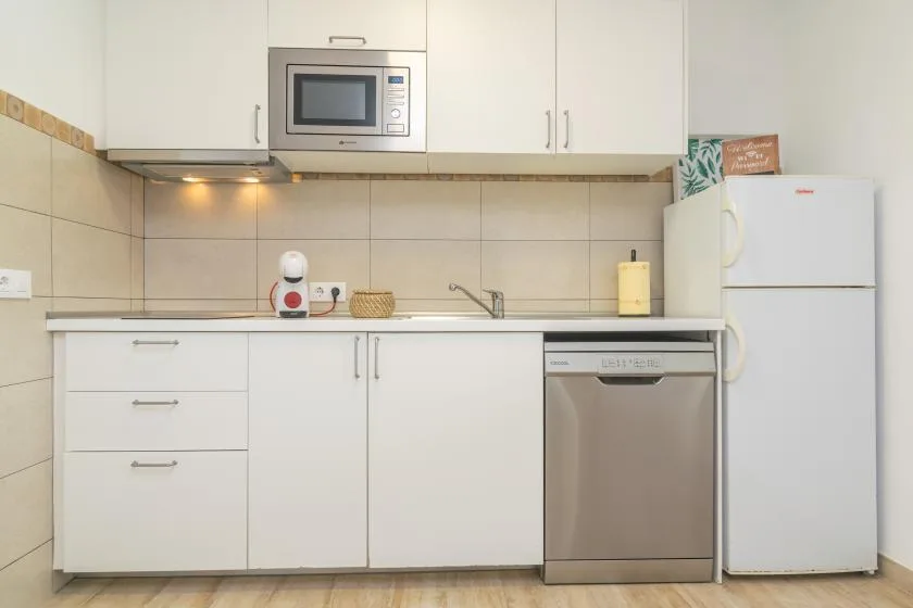 A bright kitchen with white cabinets, a refrigerator, and a stainless steel dishwasher.