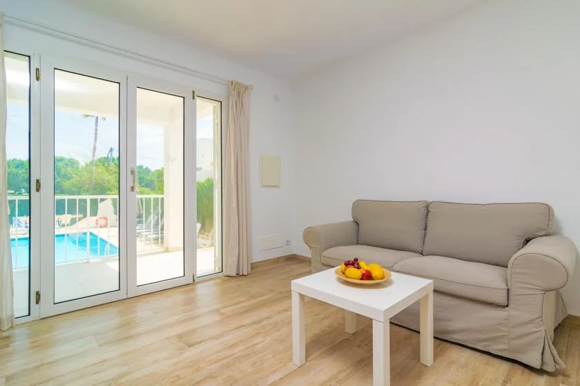 Una sala luminosa con un sofá beige y puertas de vidrio con vista a una piscina.