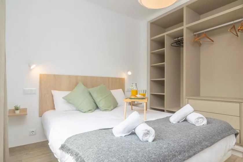 A bedroom with a white bed, green pillows, and an open wardrobe.