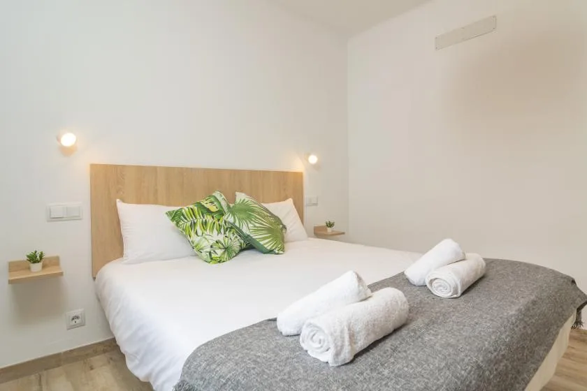 A bedroom with a bed dressed in white linens and green leaf-patterned pillows.