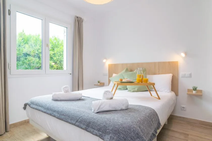 A bright bedroom with a bed, folded towels, and a tray by the window.