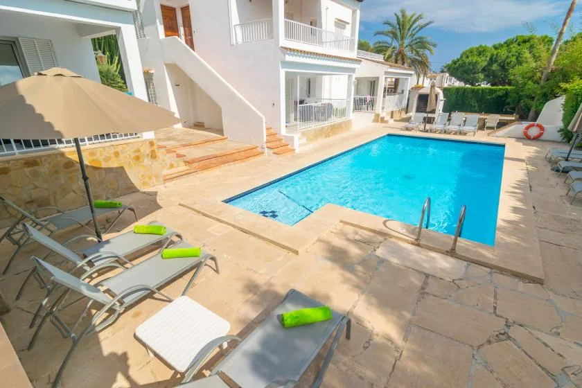 An outdoor swimming pool beside a white building, with lounge chairs on the paved deck.